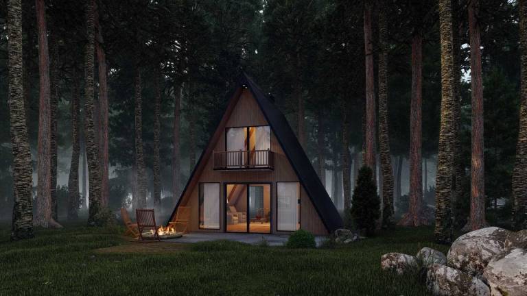modern A-frame cabin surrounded by tall trees with large glass windows and a loft balcony, illustrating an off-grid cabin design for wooded, mountain, and recreational properties
