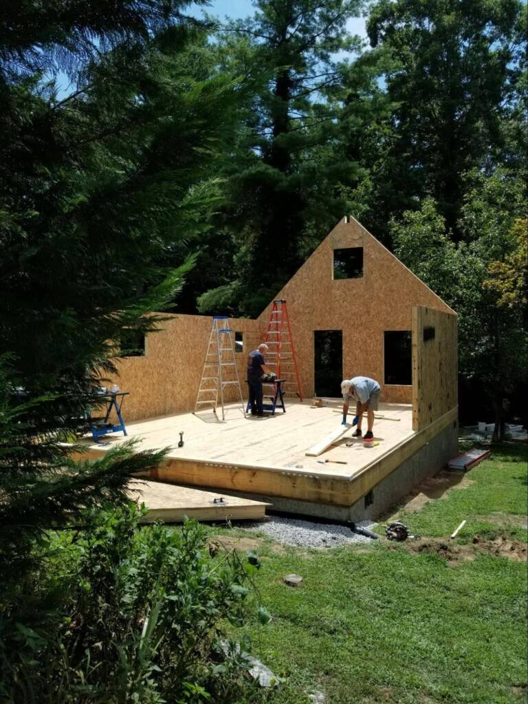 builders assembling a SIP home structure on site in a wooded area where flat-packed panels provide flexibility for limited property access conditions