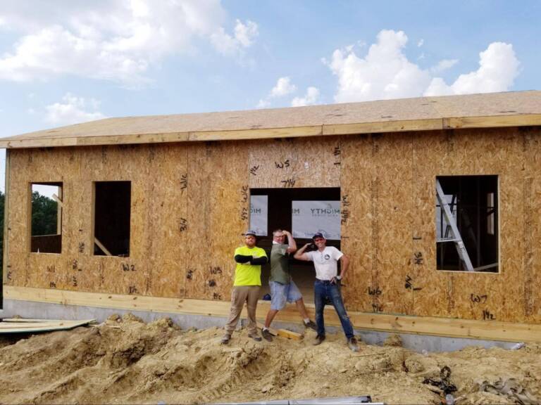 three builders standing in front of a Ranch model under construction with SIP wall panels, illustrating the assembly of a single-story home designed for efficient off-grid living