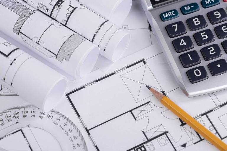 plans, calculator, and drafting tools representing cost evaluation and planning considerations when comparing SIP and modular construction methods