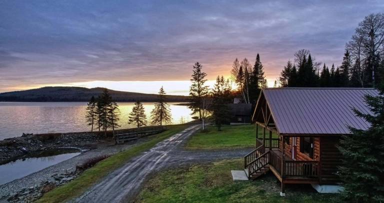 small lakeside cabin overlooking the water at sunset, illustrating the simplicity, independence, and slower pace that attract many people to off-grid living in a smaller home