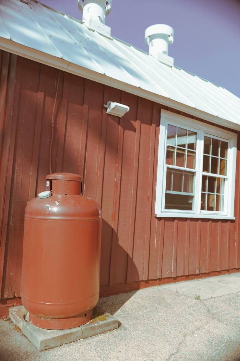 residential propane tank beside a home, illustrating a supplemental energy source for space heating, hot water, cooking, and backup power in off-grid living