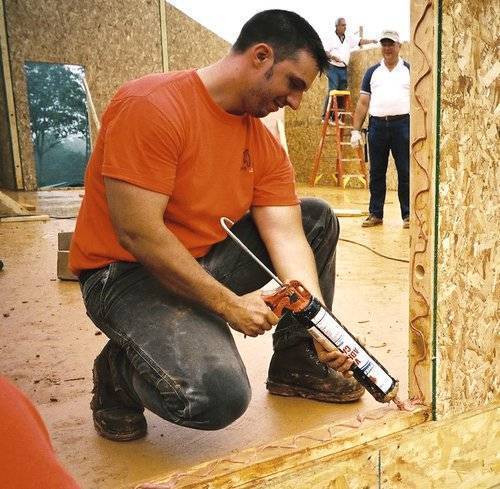 person building a small house kit putting caulk in window panel