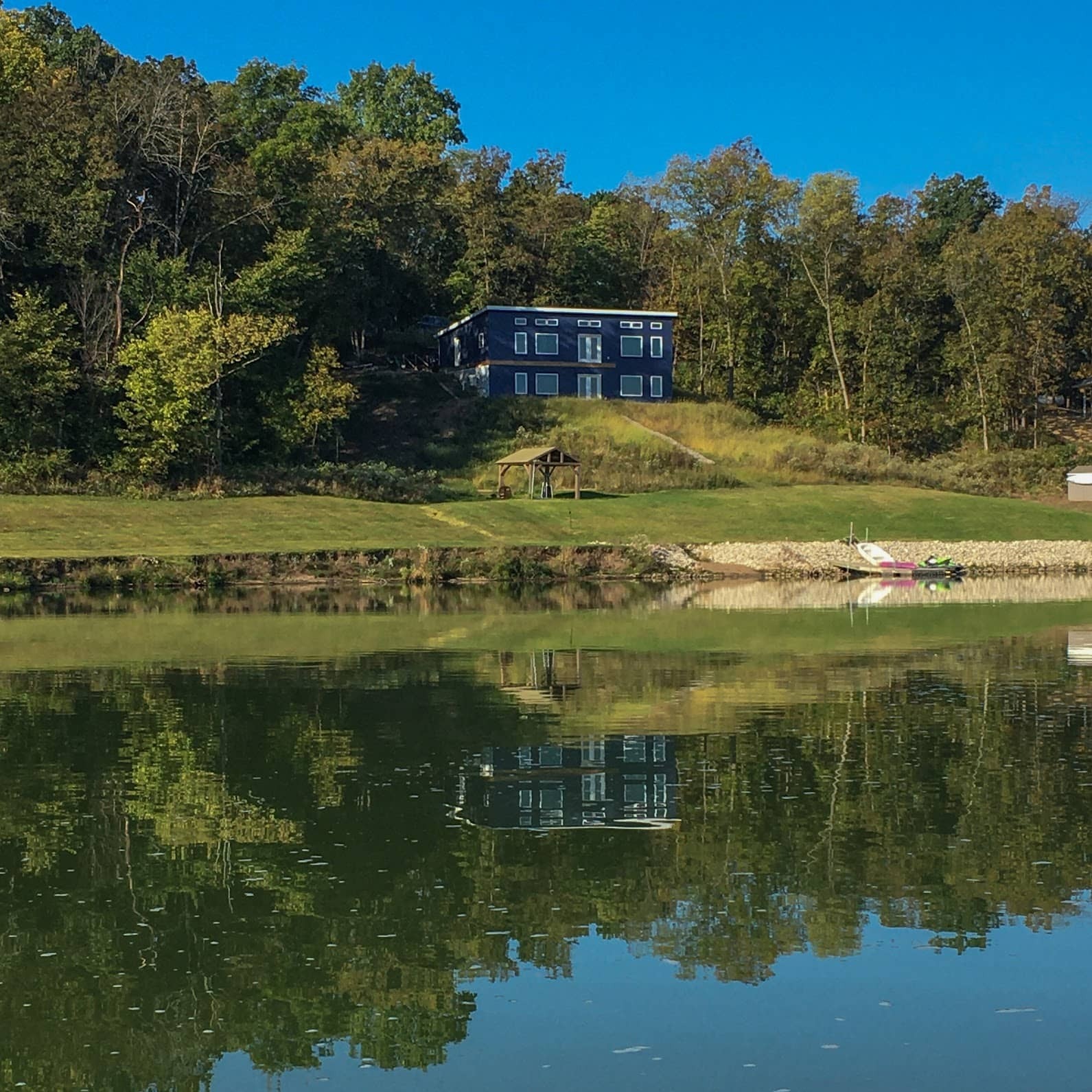 A lakehouse nestled among trees, with its reflection visible in the calm waters of the lake.
