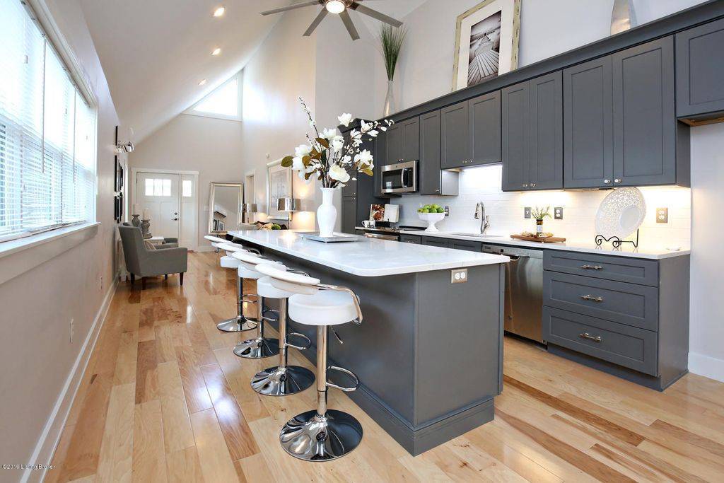 A sleek kitchen with dark cabinetry, a white island, and a row of bar stools in a bright, open layout.