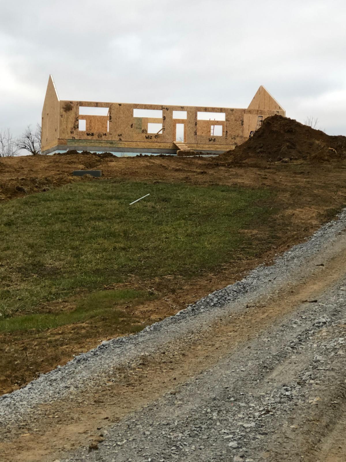 A hillside view of a wooden-framed house under construction with exterior walls erected.