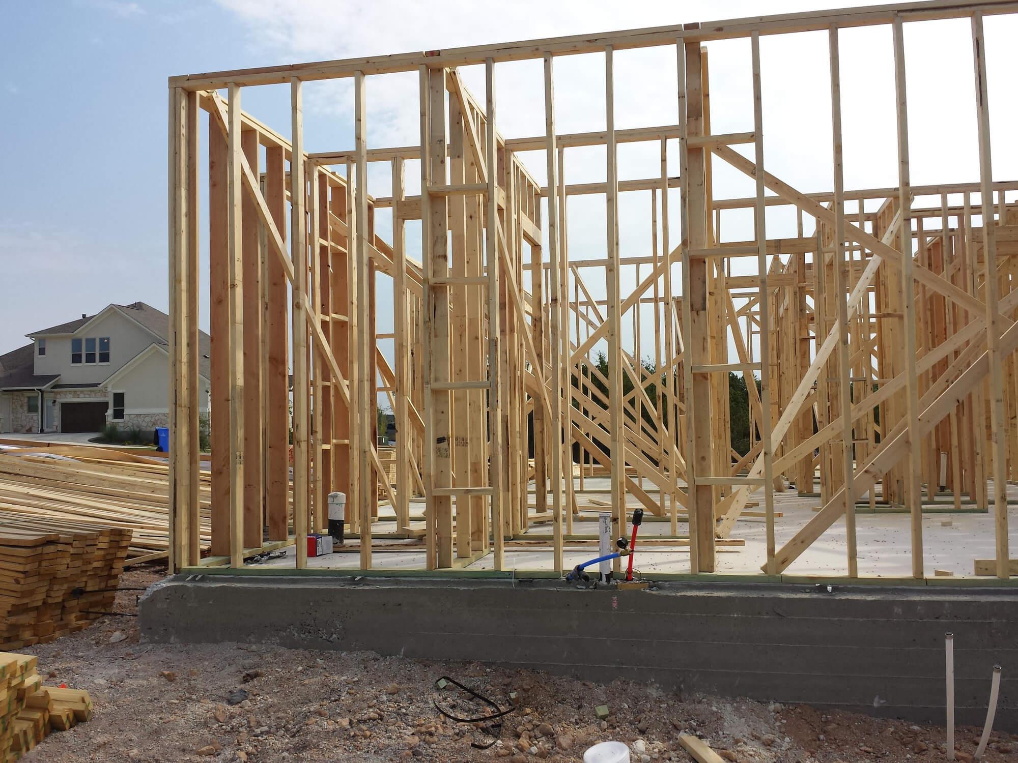 wooden framing for a house stands on an active construction site, with vertical studs and beams exposed under an open sky