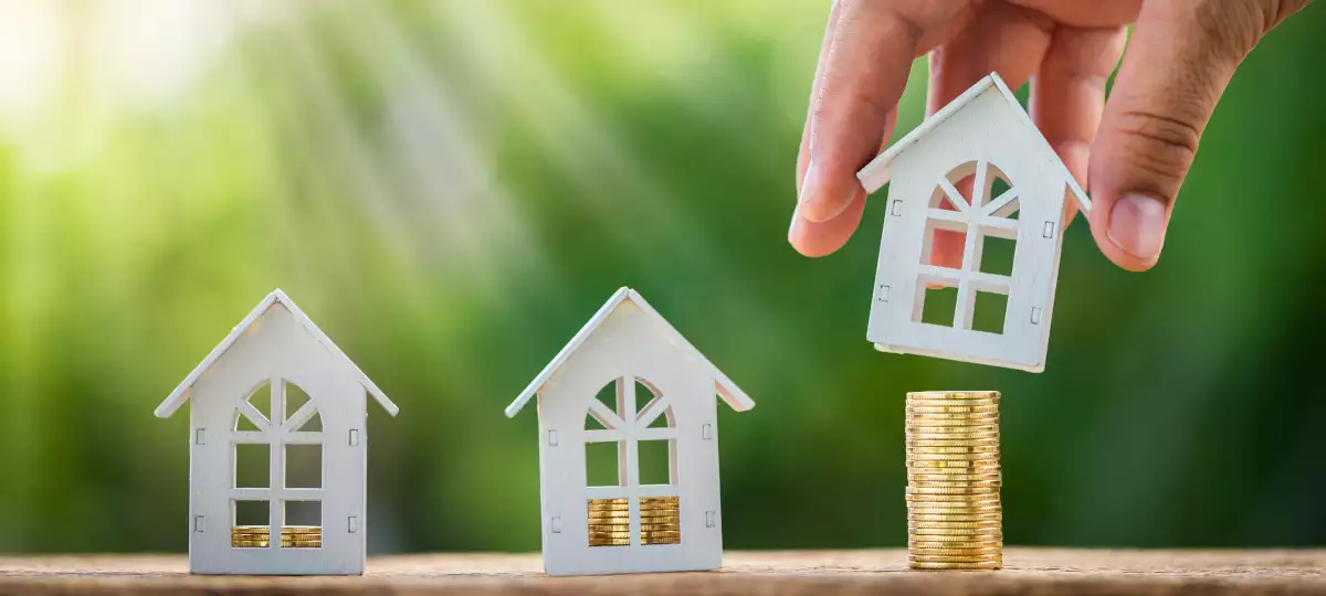 Image of a hand picking up a house sitting on a stack of coins