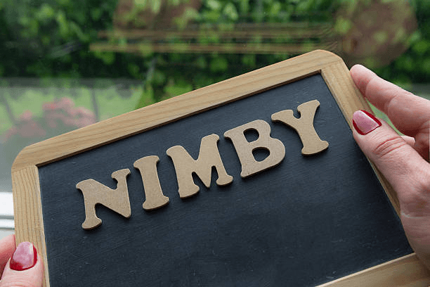 Photo of pair of hands holding a slate which reads NIMBY