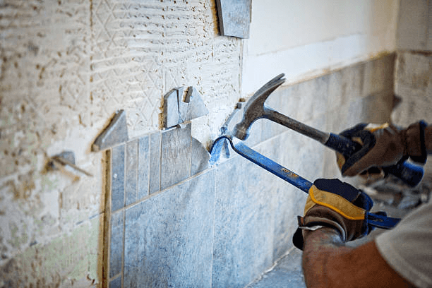 Photo of tile being torn from a wall with a hammer and crowbar