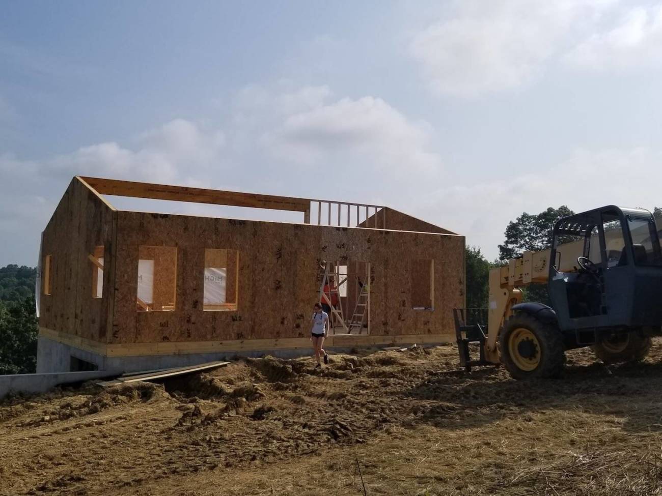 Image of young woman walking in front of the house while workers frame an interior wal