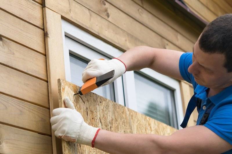 a man nailing plywood over the windows of a house to prepare for severe weather