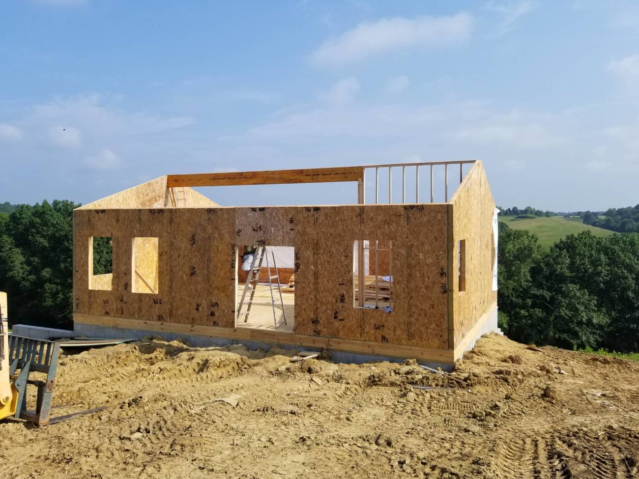Photo of the front view of a ranch house under construction with rolling hills in the background