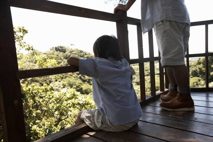 Image of a young boy sitting against the railing enjoying the view from a tree house